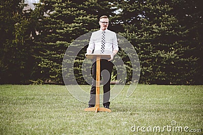 Religious person giving a speech at the tribune in a park with bright sunlight in the background Stock Photo