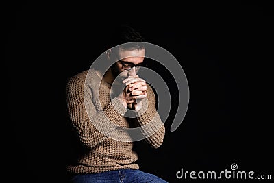 Religious young man praying to God on black background Stock Photo