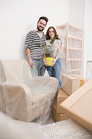 Relocating, yong couple standing in new apartment with furniture coverd with foil. Stock Photo