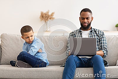 Reluctant Black Dad Ignoring Offended Son Using Laptop Indoors Stock Photo