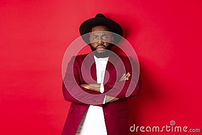Reluctant and upset Black man waiting for apology, cross arms on chest and looking offended at camera, red background Stock Photo