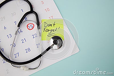 Reminder written on a sticky note to visit a doctor and stethoscope on a calendar Stock Photo