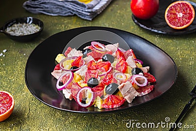 Remojon salad of blood oranges, potatoes, boiled salted fish and red onions on a black plate on a green concrete background. Stock Photo