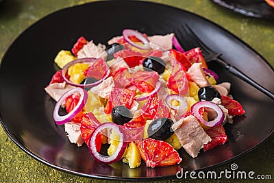 Remojon salad of blood oranges, potatoes, boiled salted fish and red onions on a black plate on a green concrete background. Stock Photo