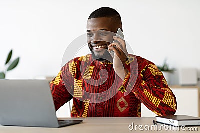 Remote Career. Young African Freelancer Man Talking On Cellphone At Home Office Stock Photo