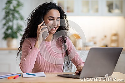 Remote Career. Young Happy Female Freelancer Using Cellphone And Laptop In Kitchen Stock Photo