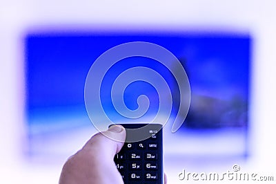 The remote control is in the hand of a man, directed to a large-screen TV Stock Photo