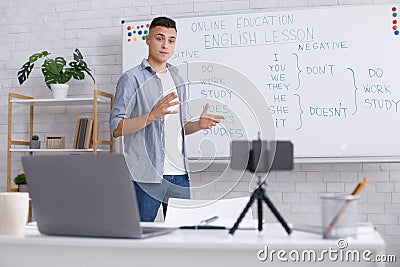 Remote education at home during epidemic. Young man explains rules of English for students, standing near blackboard and Stock Photo