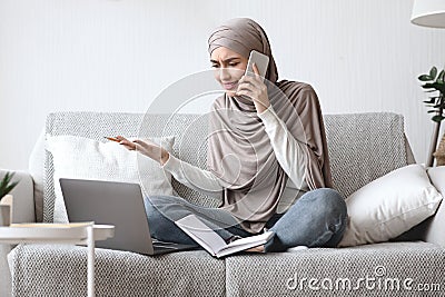 Arab woman arguing on cellphone while working on laptop at home Stock Photo