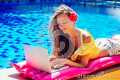 Remote work dream job.young woman sitting on inflatable pink mattress in the swimming pool having sunbath and working on Stock Photo