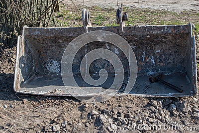 Removed from excavator metal bucket with stiffening ribs inside and eyelets on top, at bottom of bucket on right is sledgehammer Stock Photo