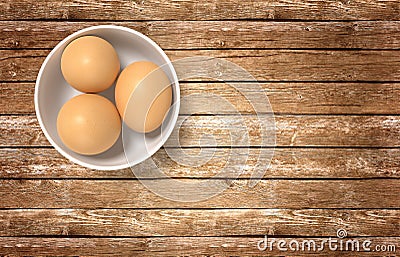 White ceramic bowl ful of eggs. Placed on wooden table. Stock Photo