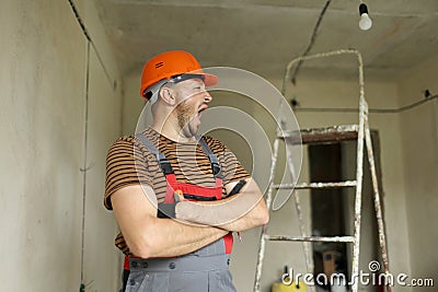 Renovation apartment. Young tired foreman constructor repairman with crossed hands in protective helmet and overalls is Stock Photo