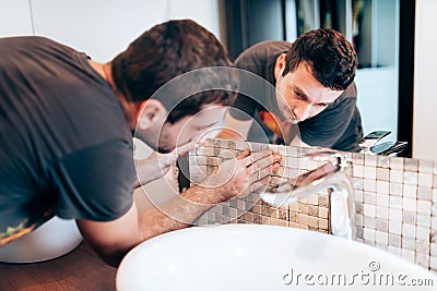 renovation details. Construction details with handyman or worker adding mosaic ceramic tiles on bathroom walls Stock Photo