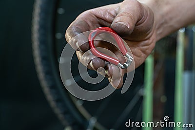 Repair bicycle wheel. Spoke key in the mechanic's hand. Rear wheel of a mountain bike on a black background. Dirty hands and Stock Photo