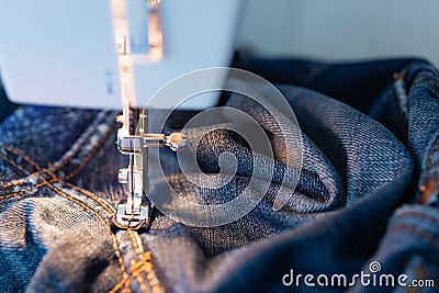 Repair jeans on the sewing machine. View of the fabric, needle and thread. Illumination from the built-in incandescent lamp. Stock Photo