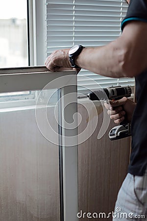 Repair of PVC windows. A worker installs a new pvc window mechanism using a drill. Selective focus, shallow depth of field Stock Photo