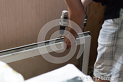 Repair of PVC windows. A worker installs a new pvc window mechanism using a drill. Selective focus, shallow depth of field Stock Photo