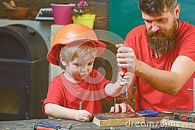 Repair and workshop concept. Boy, child busy in protective helmet learning to use screwdriver with dad. Father, parent Stock Photo