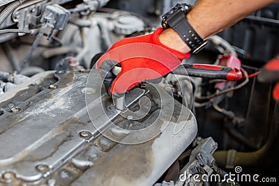 Repairing a car. An auto mechanic unscrews the gas distribution mechanism cover with a ratchet wrench Stock Photo