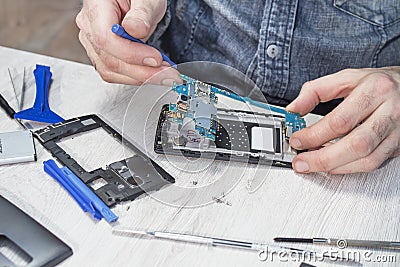 Repairing the mobile phone. The man`s hands take out the circuit board from the cell phone casing. Stock Photo