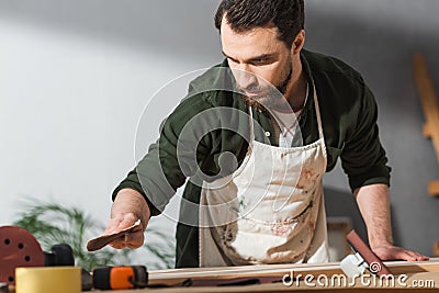 Repairman in apron holding sandpaper near Stock Photo