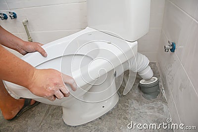 Repairman hands installing flush toilet, toilet bowl in the bathroom Stock Photo