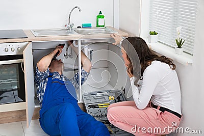 Repairman Repairing Pipe While Woman In The Kitchen Stock Photo