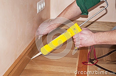 Repairman's hands Installing Skirting Board Oak Wooden Floor with Caulking Gu Stock Photo