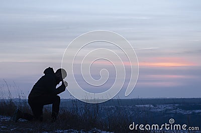 Repentance. A man on his knees. Prayer. Silhouette of a man on a blue sky background. Kneeling Prayer to God. Glorification Stock Photo