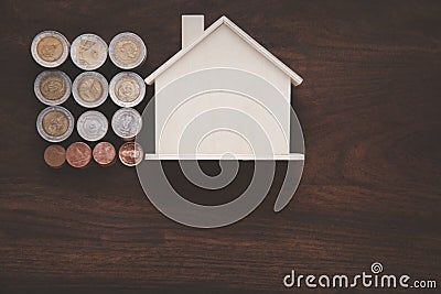 A replica wooden house and a pile of coins are placed on the old wooden floor. Stock Photo