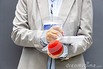 Reporter at press conference or media event, writing notes, holding microphone. Broadcast journalism concept. Stock Photo