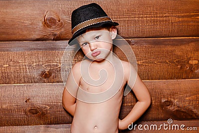 Resentful boy in hat on the background of wooden wall Stock Photo