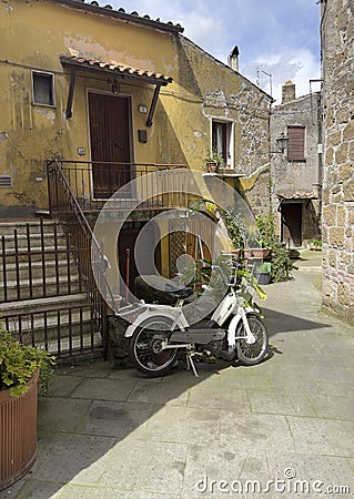 Residential street with a parked electric bicycle and potted plants in a neighborhood of Pitigliano, Italy. Editorial Stock Photo