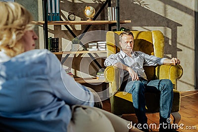 Resolute short-haired man in blue jeans sitting in front of his wife Stock Photo