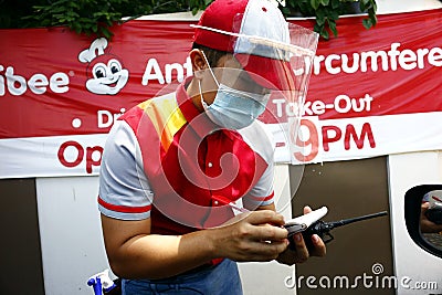 Restaurant employee with PPE serve a customer at the drive thru facility of a fast food restaurant Editorial Stock Photo