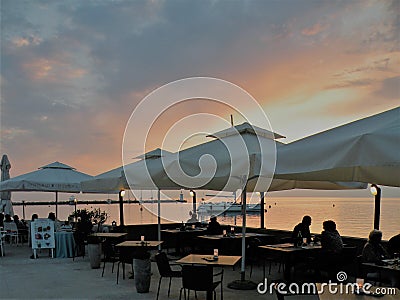 Restaurant by the sea with sunset, people at dinner, tables under white umbrellas Editorial Stock Photo