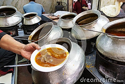 A restaurant worker spooning a mutton curry from the big pot Stock Photo