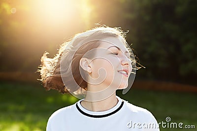 Restful attractive young female closing her eyes with pleasure admiring sunset and fresh air outdoor. Beautiful woman with waved h Stock Photo