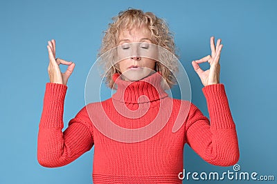 Restful blonde female in red sweater feels relaxed, tries to concentrate Stock Photo