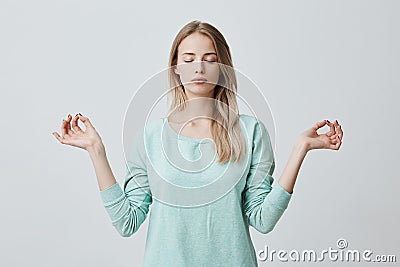 Restful peaceful blonde female feels relaxed, stands in lotus pose, tries to concentrate or to be focused, closes eyes Stock Photo