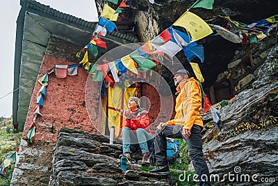 Resting Backpackers Couple tea break at small sacred Buddhist monastery decorated multicolored Tibetan prayer flags with mantras. Stock Photo