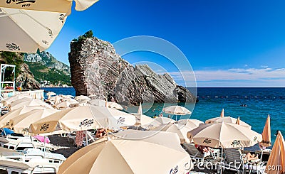 Resting people on pebble public stone beach with beautiful puff rocks. Rafailovici, Montenegro Editorial Stock Photo