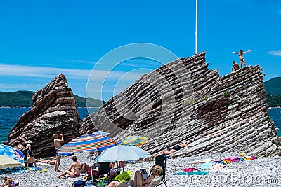 Resting people on pebble public stone beach with beautiful puff rocks. Rafailovici, Montenegro Editorial Stock Photo