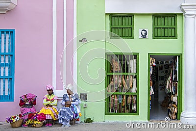 Street entertainers - flower girls - women in traditional costumes sitting in front of colorful souvenir shops, Havana, Cuba Editorial Stock Photo