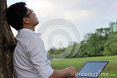 Resting time. Asian young man looking at the sky after work against his laptop. Stock Photo