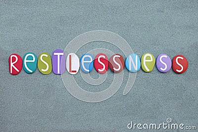 Restlessness, the inability to rest or relax, creative text composed with multi colored stone letters ovwer green sand Stock Photo