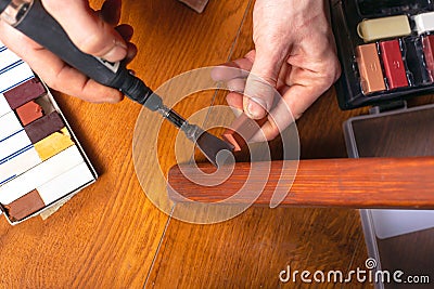 Restoration of wooden furniture. master fixes a scratch on the table leg with a wax pencil and a soldering iron close-up Stock Photo