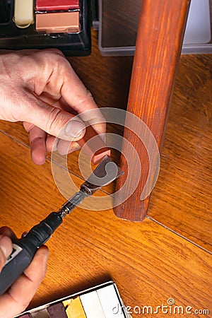 Restoration of wooden furniture. master fixes a scratch on the table leg with a wax pencil and a soldering iron close-up Stock Photo