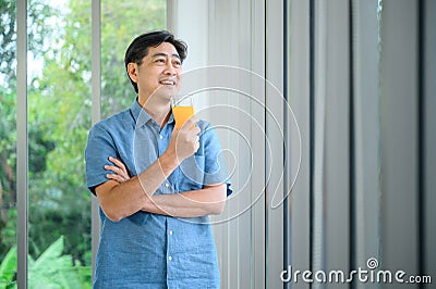 A retired Asian old man drinking orange juice, looking out the window in the morning Stock Photo